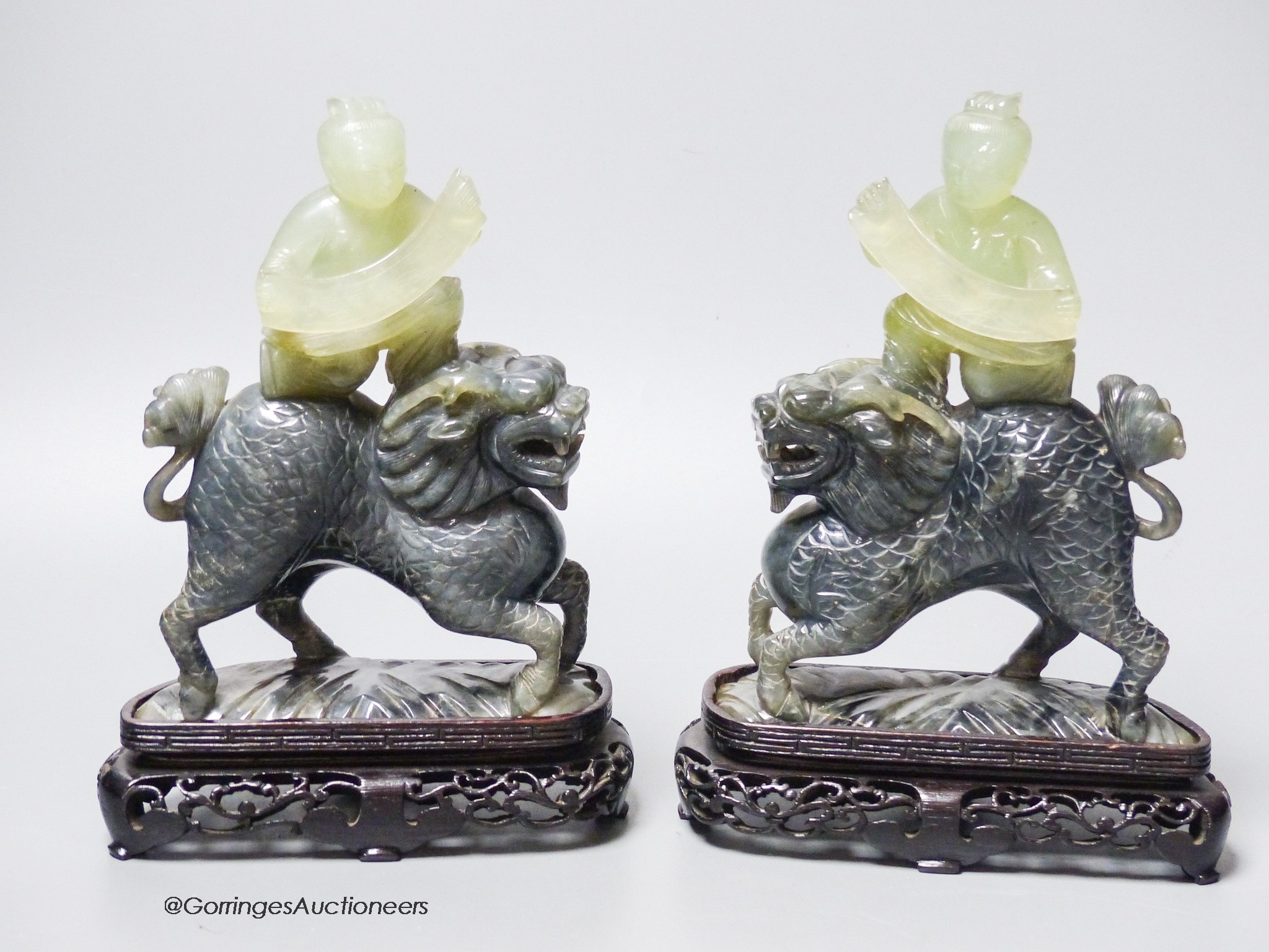 A pair of Chinese bowenite Jade figures of boys riding a qilin, mid 20th century, wood stands